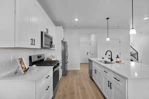 Kitchen featuring appliances with stainless steel finishes, white cabinets, light wood-style flooring, a kitchen island with sink, and tasteful backsplash