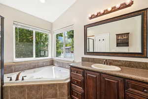 Bathroom with lofted ceiling, vanity, a jetted tub, and recessed lighting