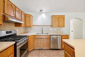 Kitchen featuring appliances with stainless steel finishes, decorative backsplash, under cabinet range hood, light countertops, and a textured ceiling