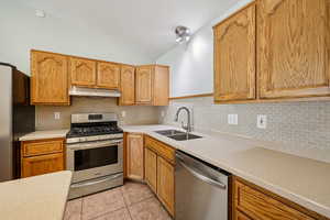 Kitchen featuring appliances with stainless steel finishes, backsplash, lofted ceiling, light countertops, and light tile patterned flooring