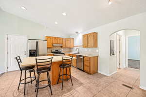 Kitchen with arched walkways, appliances with stainless steel finishes, light countertops, light tile patterned flooring, and backsplash