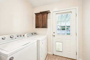 Washroom featuring cabinet space, washer and dryer, and light tile patterned floors
