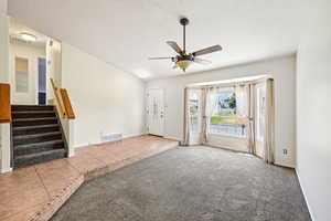 Tiled entrance foyer featuring a textured ceiling, ceiling fan, carpet flooring, and stairs