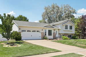 Tri-level home with brick siding, a front lawn, an attached garage, and a shingled roof