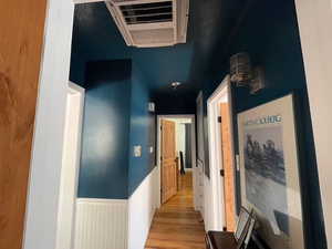 Hall featuring light wood-style flooring, cooling unit, and a wainscoted wall