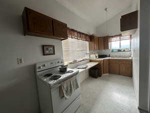 Bunk house kitchen featuring electric range, lofted ceiling, light countertops, a textured wall, and brown cabinets