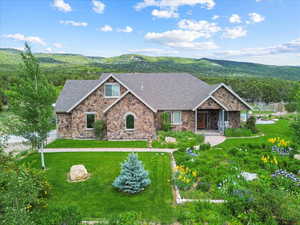 View of front of house with stone siding, a shingled roof, a mountain view, and a front yard