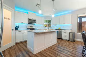 Kitchen with tasteful backsplash, white cabinets, appliances with stainless steel finishes, dark wood-style flooring, and decorative light fixtures