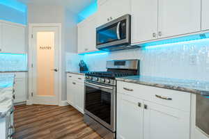 Kitchen with appliances with stainless steel finishes, white cabinetry, decorative backsplash, light stone countertops, and dark wood-type flooring