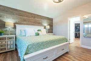 Bedroom with wood walls, wood finished floors, a walk in closet, and an accent wall
