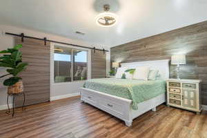 Bedroom featuring a barn door, wooden walls, and wood finished floors