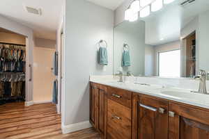 Bathroom with double vanity, a spacious closet, wood finished floors, and a stall shower