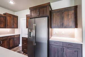 Kitchen featuring backsplash, stainless steel fridge with ice dispenser, light countertops, dark brown cabinets, and wood finished floors