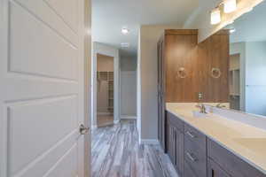 Bathroom featuring double vanity, wood finished floors, a spacious closet, and recessed lighting
