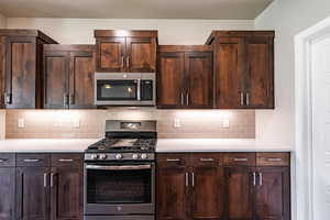 Kitchen featuring appliances with stainless steel finishes, decorative backsplash, light countertops, and dark brown cabinets