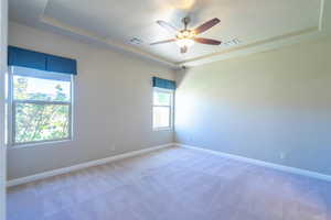 Unfurnished room with a tray ceiling, light carpet, a textured ceiling, and a ceiling fan