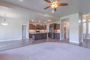 Kitchen featuring open floor plan, wood finished floors, stainless steel appliances, a ceiling fan, and a center island with sink