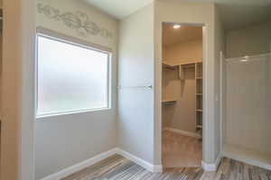 Full bath featuring wood finished floors, a spacious closet, and a shower