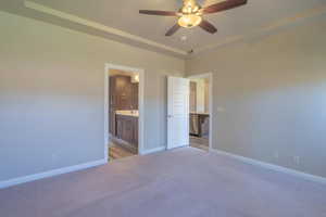Unfurnished bedroom with carpet floors, connected bathroom, a raised ceiling, and ceiling fan