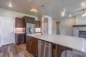 Kitchen featuring decorative backsplash, appliances with stainless steel finishes, light countertops, open floor plan, and decorative light fixtures