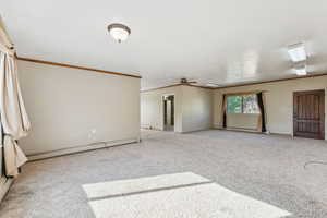 Carpeted spare room featuring crown molding, a baseboard heating unit, and ceiling fan