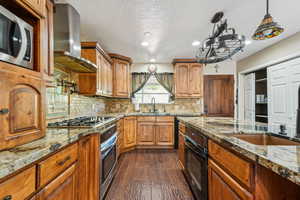 Kitchen with range hood, appliances with stainless steel finishes, dark wood-style flooring, recessed lighting, and light stone countertops