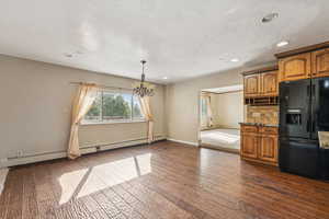Kitchen with black fridge, brown cabinets, a chandelier, backsplash, and dark wood-type flooring