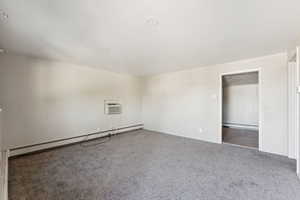 Carpeted spare room with baseboard heating, a baseboard heating unit, and an AC wall unit