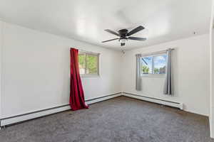Carpeted empty room featuring healthy amount of natural light, baseboard heating, and ceiling fan