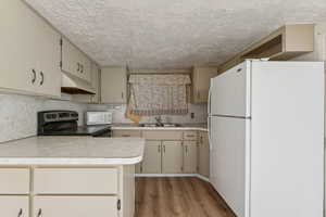 Kitchen with white appliances, tasteful backsplash, wood finished floors, light countertops, and under cabinet range hood
