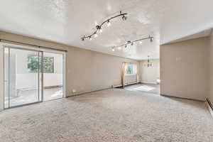Spare room featuring a textured ceiling, carpet, a baseboard radiator, a chandelier, and rail lighting