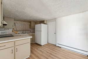 Kitchen featuring baseboard heating, white appliances, light countertops, light wood-style floors, and a textured ceiling