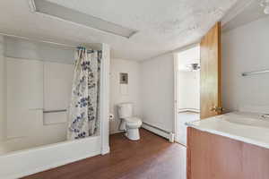 Bathroom with a textured ceiling, baseboard heating, vanity, shower / tub combo with curtain, and wood finished floors