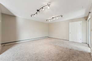 Carpeted empty room featuring a baseboard heating unit and a textured ceiling