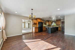 Kitchen with a chandelier, brown cabinetry, decorative backsplash, a breakfast bar area, and a center island with sink