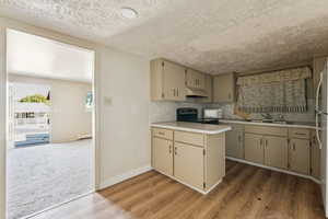 Kitchen with light countertops, white appliances, wood finished floors, decorative backsplash, and under cabinet range hood