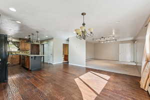 Kitchen featuring open floor plan, brown cabinets, dark wood-type flooring, freestanding refrigerator, and a chandelier