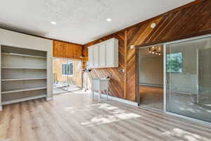 Unfurnished living room with a textured ceiling, wooden walls, light wood-type flooring, recessed lighting, and crown molding