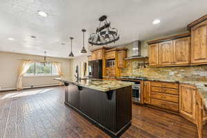Kitchen with tasteful backsplash, a breakfast bar area, a center island with sink, light stone countertops, and wall chimney exhaust hood