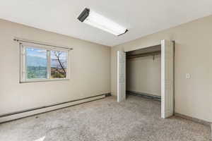 Unfurnished bedroom with a baseboard heating unit, light colored carpet, a closet, baseboard heating, and a textured ceiling