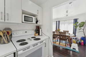 Kitchen featuring white appliances, light countertops, white cabinetry, dark wood-style floors, and backsplash