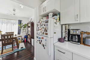 Kitchen with light countertops, freestanding refrigerator, white cabinets, and dark wood-type flooring