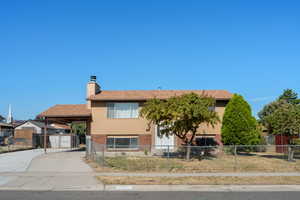 View of front of property featuring driveway, brick siding, a chimney, and a fenced front yard