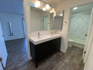 Bathroom featuring double vanity, wood finished floors, and washtub / shower combination