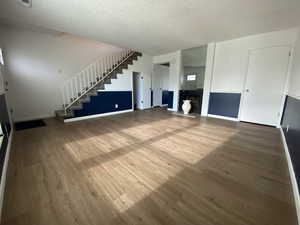 Unfurnished living room featuring stairway, wood finished floors, a textured ceiling, and a brick fireplace