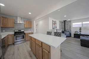 Kitchen featuring open floor plan, a wood stove, stainless steel range with gas cooktop, light countertops, and wall chimney exhaust hood