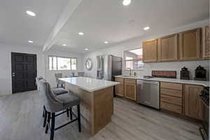 Kitchen with a kitchen bar, a center island, stainless steel appliances, light wood-style flooring, and light countertops