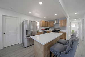 Kitchen featuring appliances with stainless steel finishes, light wood-style flooring, light countertops, a kitchen island, and recessed lighting