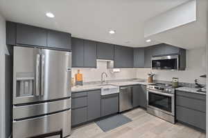 Kitchen with stainless steel appliances, recessed lighting, light wood-style flooring, light stone countertops, and gray cabinets