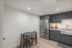 Kitchen with stainless steel fridge, light wood-type flooring, recessed lighting, light stone counters, and gray cabinetry